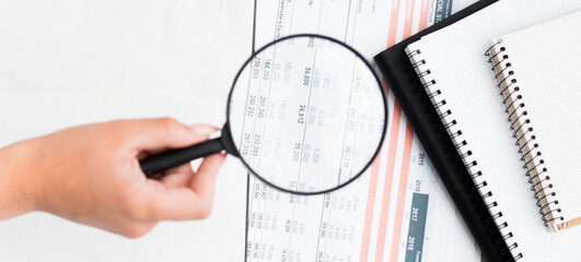 Businesswoman holding a magnifying glass on a financial report concept for finance, balance sheet, tax or accounting