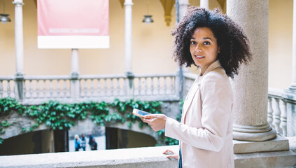 Glad ethnic tourist with smartphone on balcony