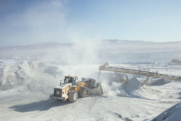 Wheel front-end loader working in a cloud of dust in sunny weather at a mining enterprise. Mining...