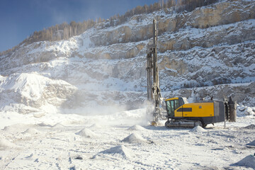 Drilling machine works in a snow-covered stone quarry in a winter sunny day. Mining industry.