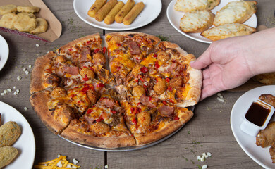 Hand handing out a slice of barbecue pizza. Pizza party. Italian meat pizza on wooden background.