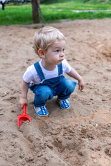 A little boy of two years in a blue jumpsuit and a white T-shirt walks in the park and is surprised by everything that is happening around him. High quality photo