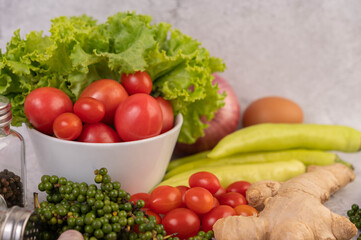 Lettuce and tomatoes in a white cup with sliced ​​onions and fresh peppers on the cement floor.