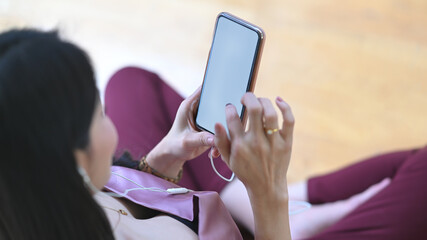 The top view image of a woman is relaxing with a white blank screen smartphone in the living room.