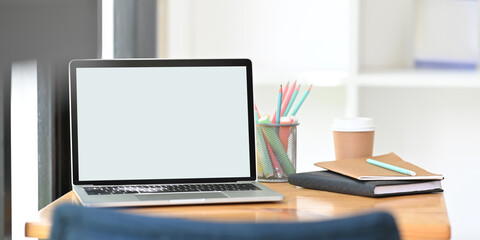 A wooden working desk is surrounding by a computer laptop and personal stuff.