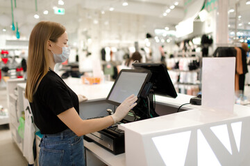 Girl seller in a mask and gloves stands at the checkout in a store. Store seller during COVID-19....