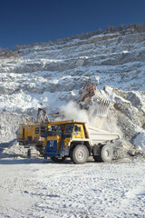 Big mining excavator and big mining dumping truck in a snow-covered stone quarry, loading the stone ore. © esalienko