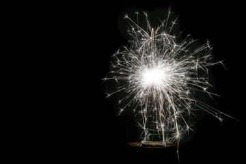 Happy New Year, festive, white sparkling burning sparkler or salute on a black background. Holiday concept, copy space.
