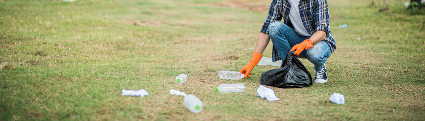 A man wearing orange gloves collecting garbage in a black bag.