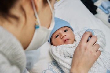 young redheaded mother with preventive health mask and lgtbiq+ bracelet, next to her newborn baby...
