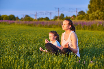 Naklejka na ściany i meble a mother and her child do yoga in the fresh air. The concept of a healthy lifestyle. Outdoor recreation. Meditation and yoga classes