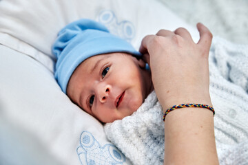 beautiful and adorable newborn baby lying on the bed smiling and being caressed by the mother with an lgbtiq + bracelet