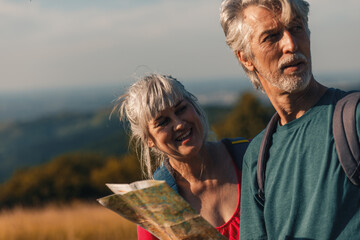 Active senior couple hiking in nature with backpacks, enjoying their adventure at sunset.