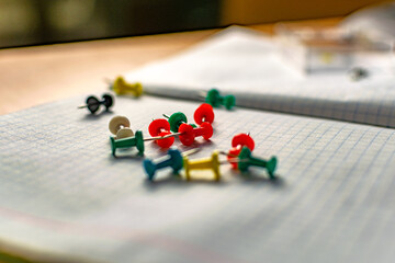 Colored small office buttons with different convenient protective hats, modern office details scattered on notebook leaves in a check