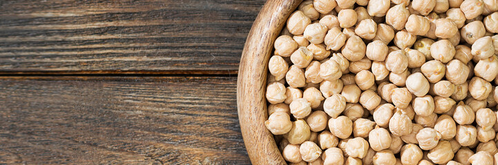 Chickpeas in a wooden bowl on the brown kitchen table. Raw chickpeas close-up. Banner with space...