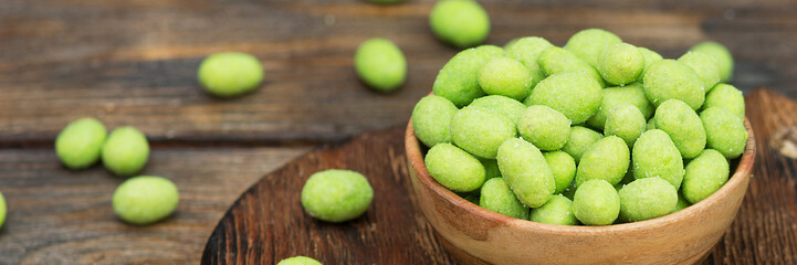 Fried peanuts in wasabi in a wooden bowl on a brown wooden table. Banner with space for text - obrazy, fototapety, plakaty