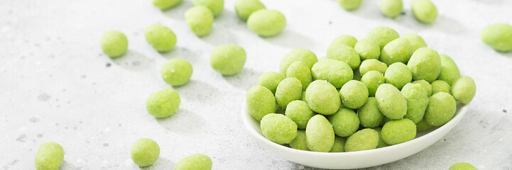 Fried peanuts in wasabi in a white bowl on a light gray table. Banner with space for text - obrazy, fototapety, plakaty