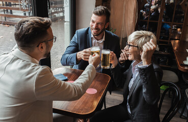 Senior businesswoman sitting with her younger male colleagues at cafe taking a brake and drinking beer.