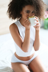 Good morning. Pretty afroamerican model with cup of coffee start a day in a bed.