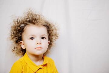 Little cute girl with blond curly hair and big beautiful eyes dressed in a yellow dress