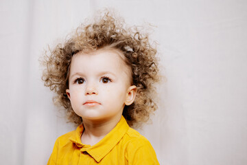 Fototapeta premium Little cute girl with blond curly hair and big beautiful eyes dressed in a yellow dress