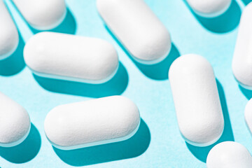 White tablets on a light pastel blue table. Repeated pills on a blue background. Macro