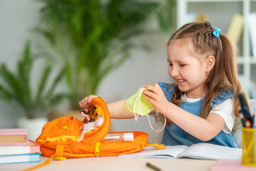 Cute funny little girl packs a backpack for school, puts a mask on.