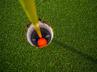The orange golf ball falls into the hole.