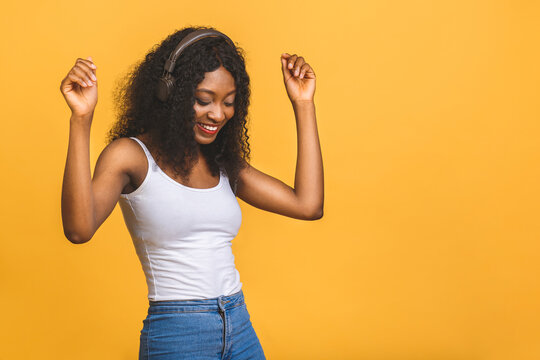 Studio photo of inspired african american lady listening music, dancing with eyes closed. Indoor portrait of relaxed black girl isolated on yellow background.