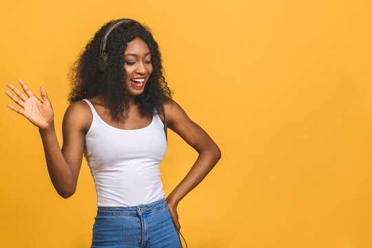 Studio photo of inspired african american lady listening music, dancing with eyes closed. Indoor portrait of relaxed black girl isolated on yellow background.