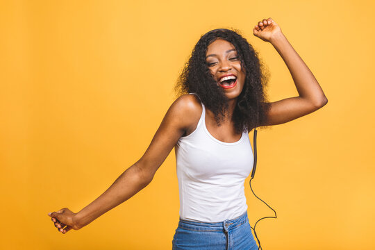 Studio photo of inspired african american lady listening music, dancing with eyes closed. Indoor portrait of relaxed black girl isolated on yellow background.