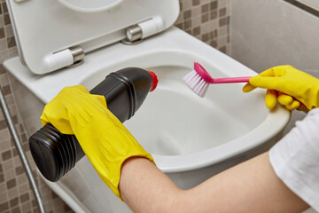 Cleaning a white toilet with household chemicals and a pink little brush..