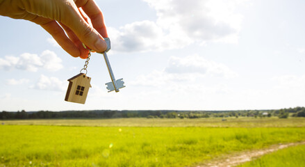 Wooden pendant of a house and key. Background of the sky and field. Dream of home, building a...