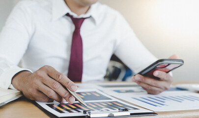 Young Asian businessman calculates graph data through his mobile phone in his office.