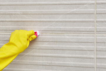 Close-up hand of professional maid cleaning tile seam in bathroom. Rubber gloves