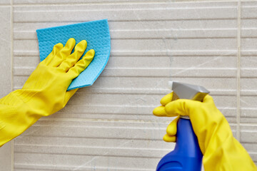 Female hand in a protective glove with a napkin for cleaning and a spray.