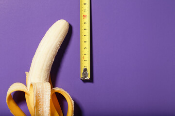 Yellow banana penis concept measured by measuring tape on a purple background. - obrazy, fototapety, plakaty