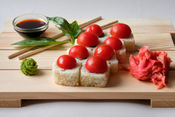 Japanese sushi rolls with cherry tomatoes, wasabi, ginger and soy sauce on the wooden board. Tasty food.
