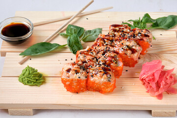 Japanese Red sushi rolls with orange masago, eel, prawns, wasabi, omelette, soy sauce, and pickled ginger. Tasty and artistic food for restaurant or cafe menu. Roll on wooden board.