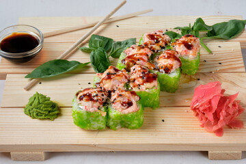 Japanese sushi Tobiko rolls with Sweet sauce, wasabi, soy sauce, basil leaves and marinated ginger. Tasty and artistic food for restaurant or cafe menu. Roll on the wooden board. Food photography.