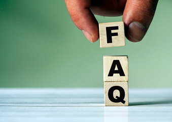 The hand puts the cube block with the inscription FAQ. FAQ concept and background.