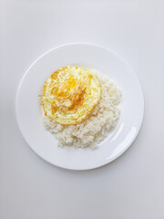 Fried egg or overcooked sunny side up, served with white rice, on a white plate, isolated in white background