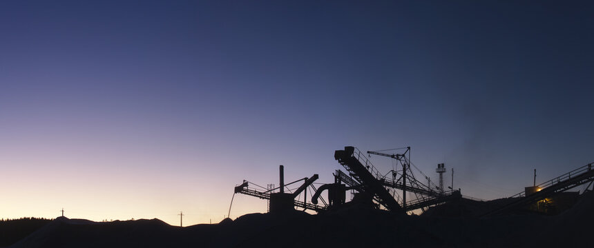 Silhouettes of stone crushing equipment of mining and processing plant on the background of the sunset sky in cold lilac tones, panorama.