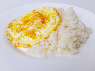 Fried egg or overcooked sunny side up, served with white rice, on a white plate, isolated in white background