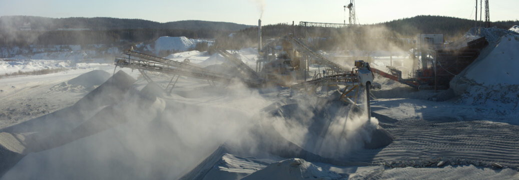 Panoramic image of working stone crushing equipment in a dust cloud at a mining and processing plant, close-up.
