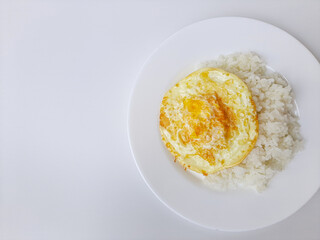 Fried egg or overcooked sunny side up, served with white rice, on a white plate, isolated in white background