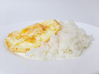 Fried egg or overcooked sunny side up, served with white rice, on a white plate, isolated in white background