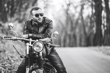 Bearded brutal man in sunglasses and leather jacket sitting on a motorcycle on the road in the...