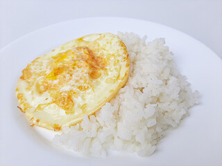 Fried egg or overcooked sunny side up, served with white rice, on a white plate, isolated in white background