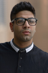 Face of young handsome Indian man with eyeglasses thinking in the city